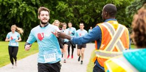 White bearded man wearing blue Run for Woment-shirt being handed water at a race by a black man in an orange safety vest