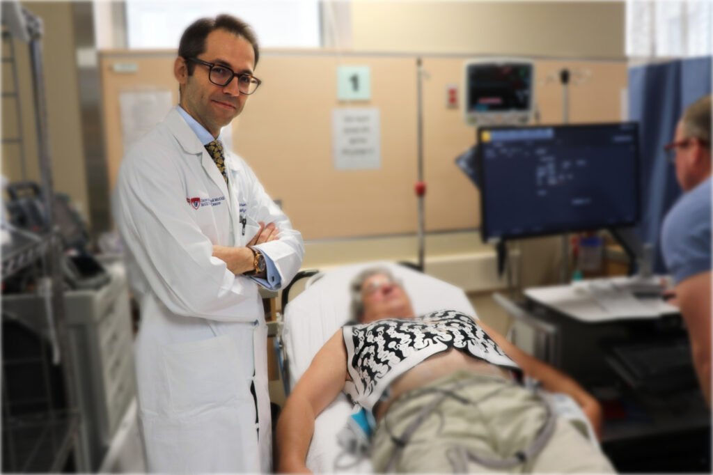 Dr. Martin Bernier of the Montreal General Hospital, standing next to a man in a gurney wearing the CardioInsight mapping vest for arrhythmias. Next to them is another man looking at data on a computer screen.