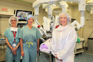 Three women in front of a surgical robot in an operating room at the Montreal General Hospital.