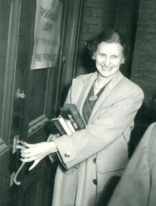 Black and white photo of a woman holding a door handle outside the Fraser-Hickson library: an example of legacy giving.
